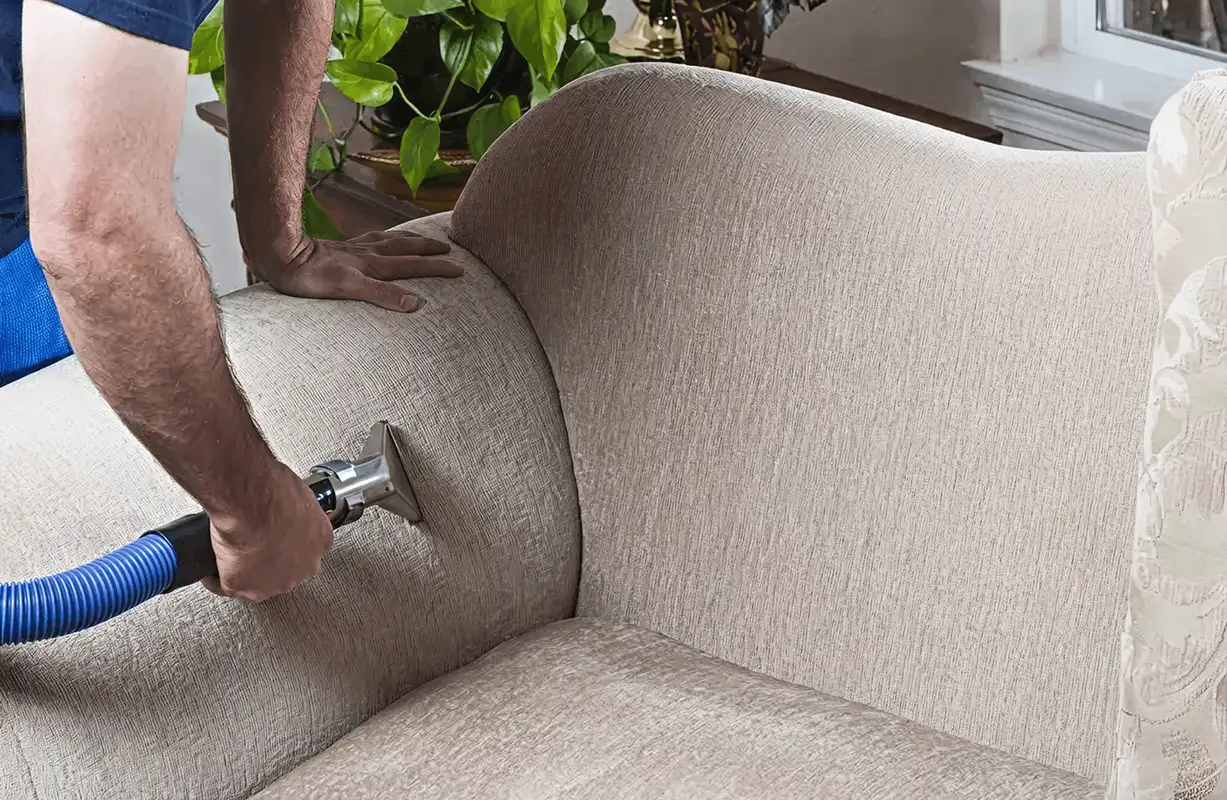Professional upholstery cleaner deep-cleaning a fabric sofa with a handheld extraction tool and hose, Allentown, PA.